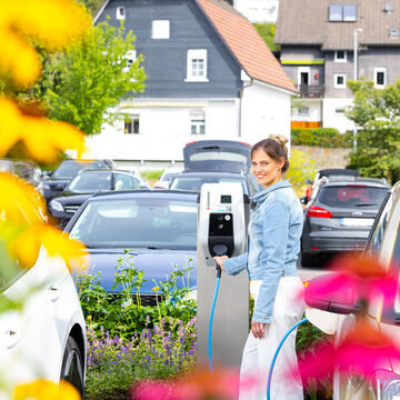 Kundin lädt ihr Elektroauto auf einem Parkplatz an einer MENNEKES Wallbox 